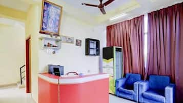 A room with a reception desk, a ceiling fan, a large window with curtains, and a blue sofa.