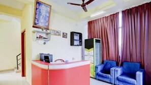 Una habitación con mostrador de recepción, ventilador de techo, ventana grande con cortinas y un sofá azul.