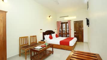 A hotel room with a bed, a desk, two chairs, a wooden bench, a television, and a window with curtains.