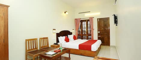 A hotel room with a bed, a desk, two chairs, a wooden bench, a television, and a window with curtains.