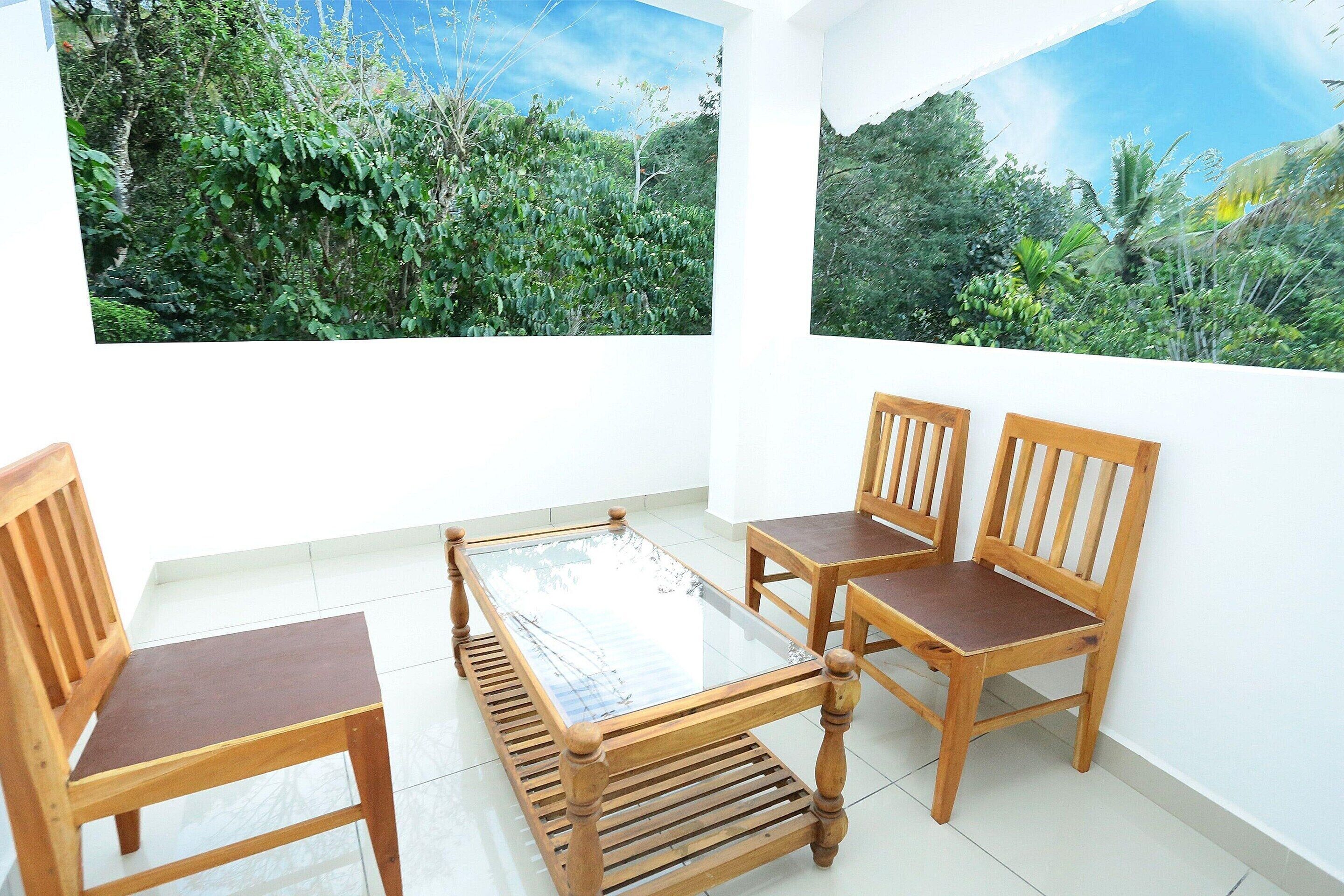 A room with a glass table surrounded by wooden chairs, white walls, and two large windows with tropical views.