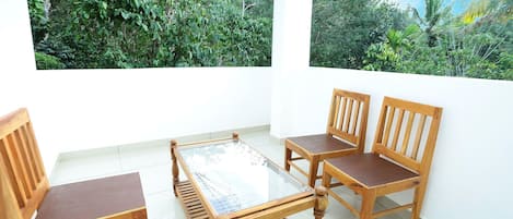 A room with a glass table surrounded by wooden chairs, white walls, and two large windows with tropical views.