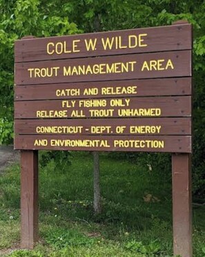 A wooden sign with text indicating it is a Cole W. Wilde Trout Management Area, with catch and release fishing only, fly fishing only, and all trout unharmed.