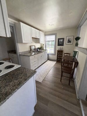 A kitchen with white cabinets, granite countertops, and a dining area with a wooden table and chairs.