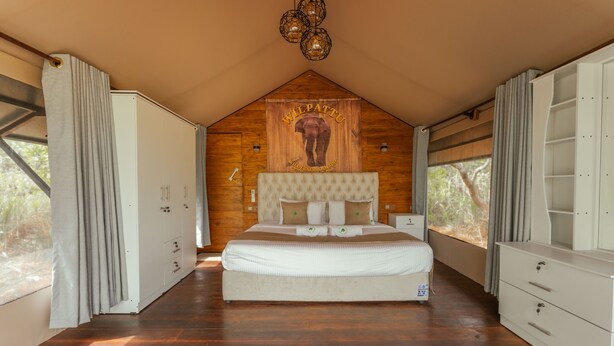 A bedroom with a large bed, wooden walls, a ceiling light fixture, and a window with curtains.
