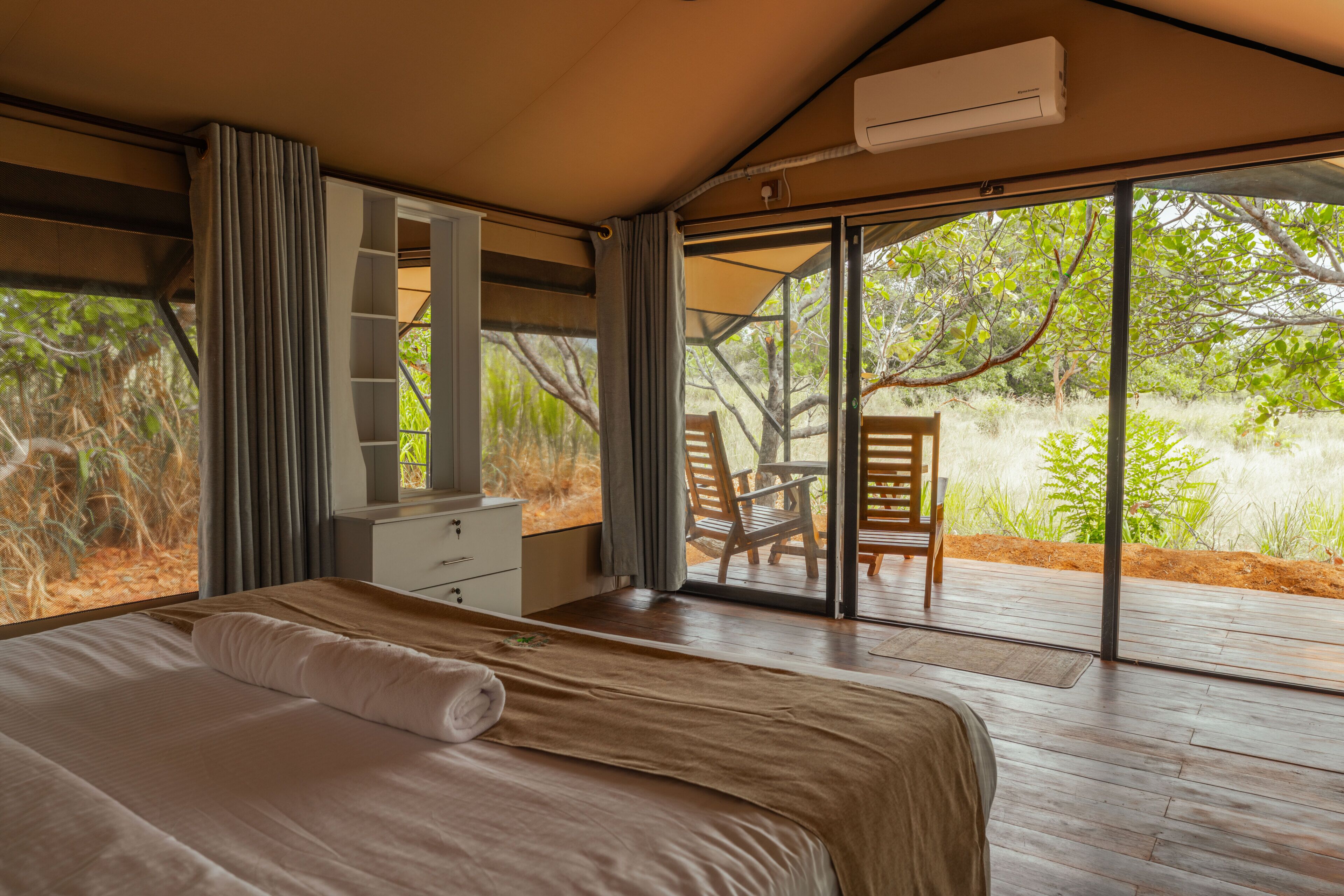 A bedroom with a bed, a desk, and a chair, with a view of greenery outside.