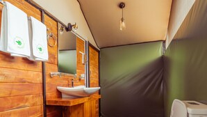 Ein kleines Badezimmer im Zeltstil mit einem hölzernen Waschtisch, einem Waschbecken und einer Toilette.