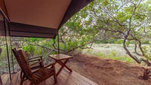 A wooden deck with a table and chairs, overlooking a natural landscape with trees and grass.