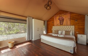 A spacious bedroom with a large bed, wooden walls, and a view of trees through a window.