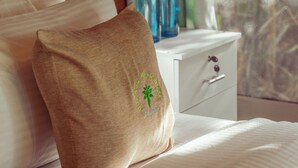 Ein ordentlich bezogenes Bett mit Kissen, ein Nachttisch mit zwei Flaschen und ein Fenster mit Vorhängen.