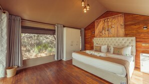 A spacious bedroom with a large bed, wooden walls, and a view of greenery outside.