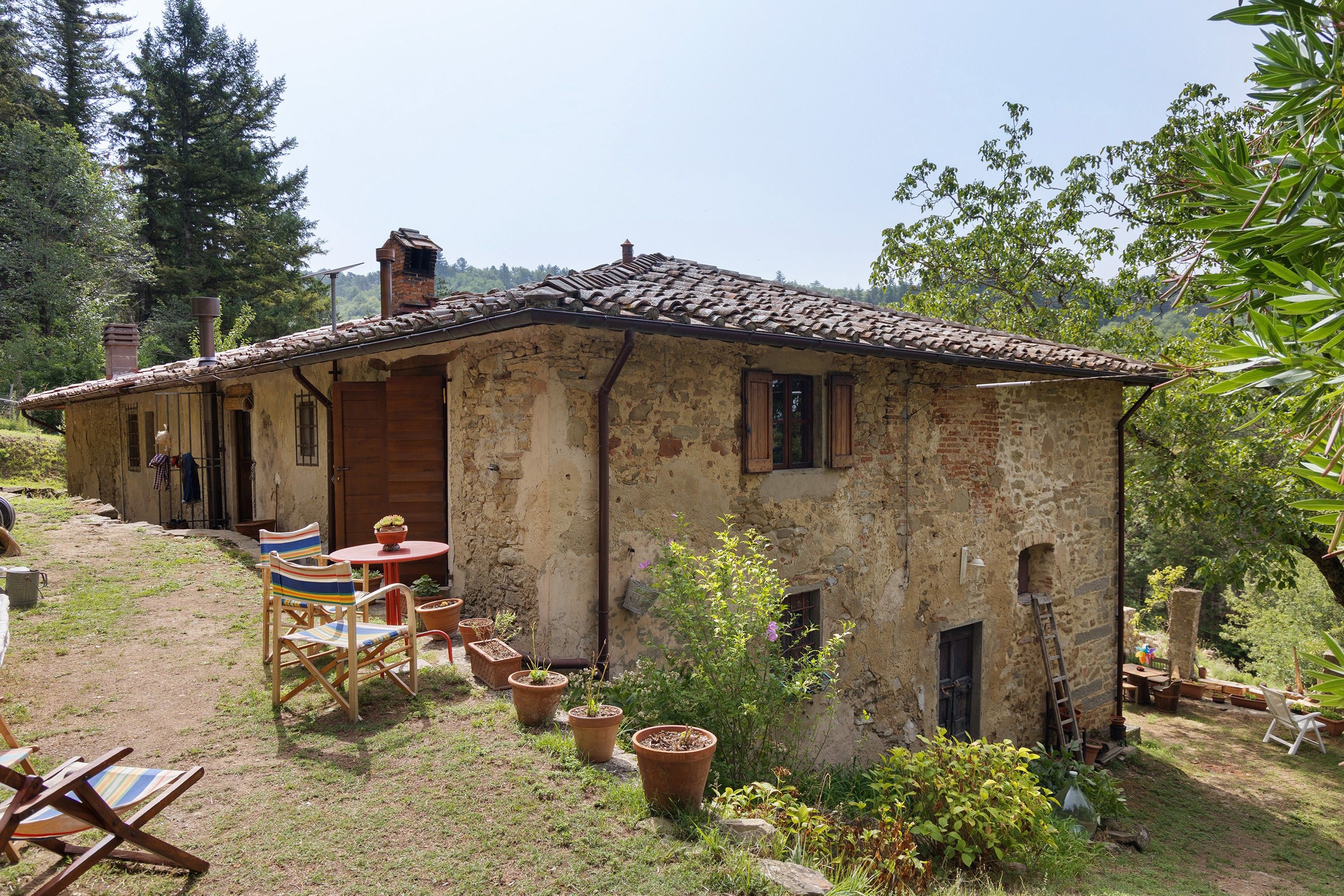 Una rustica casa in pietra con tetto in tegole, un piccolo patio con tavolo e sedie, e vasi con piante.