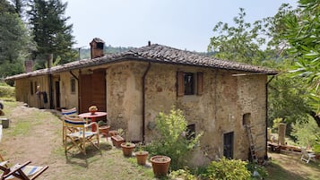 Una rustica casa in pietra con tetto in tegole, un piccolo patio con tavolo e sedie, e vasi con piante.