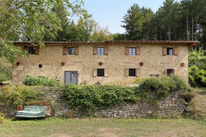 Un bâtiment en pierre doté de nombreuses fenêtres et d’une porte, entouré de verdure et d’arbres.