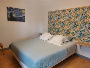 A bedroom with a bed, a nightstand, a lamp, a painting on the wall, and a floral-patterned headboard. - Château le Mas Vacation Rental with Pool: Ideal for Families, a Haven of Peace in the Castle Grounds (ST MARTIAL D ARTENSET)