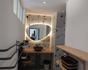 A bathroom with a large mirror, a sink, a towel rack, a trash bin, and a wooden shelf. - Château le Mas Vacation Home with Pool: Ideal for Families, a Serene Oasis in the Castle Grounds (ST MARTIAL D ARTENSET)
