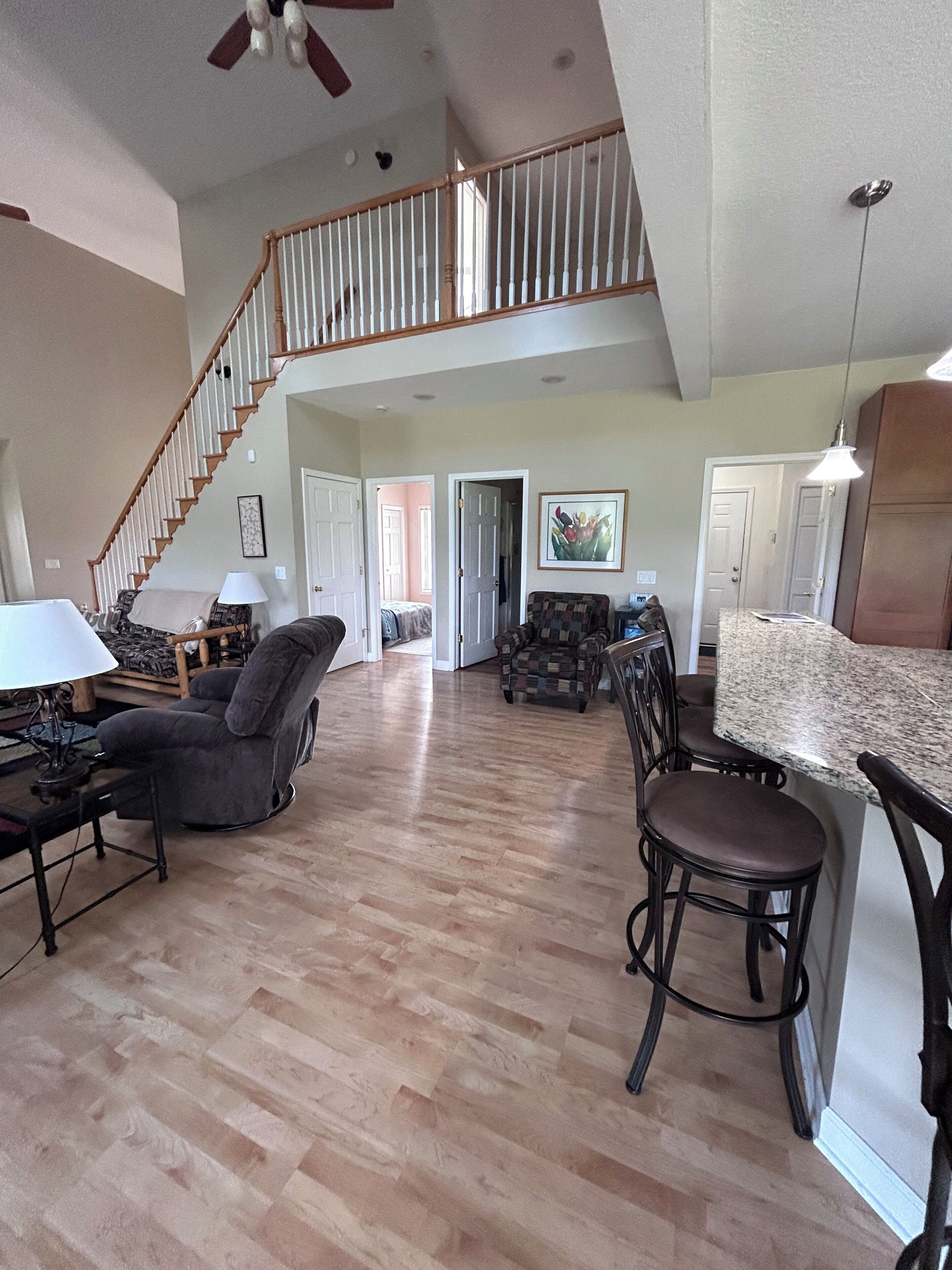 A spacious living area with a high ceiling, a staircase leading to an upper level, and a kitchen area with a granite countertop.