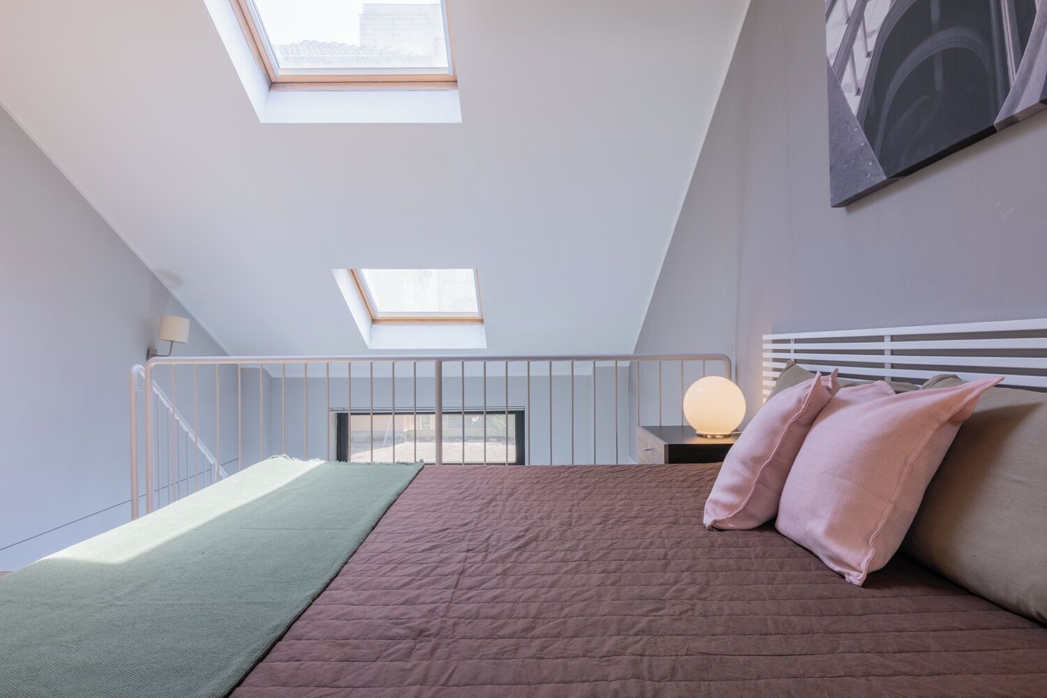 Une chambre avec une lucarne, un lit avec des oreillers roses, une lampe de chevet et une vue sur l’extérieur.