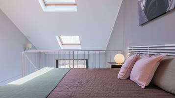 Une chambre avec une lucarne, un lit avec des oreillers roses, une lampe de chevet et une vue sur l’extérieur.