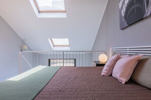 Ein Schlafzimmer mit Dachfenster, einem Bett mit rosa Kissen, einer Nachttischlampe und Blick ins Freie.