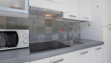 Una cocina moderna con microondas integrado, pileta de acero inoxidable y salpicadero de azulejos grises.