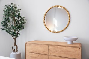 Un aparador de madera con un cuenco blanco encima, un espejo montado en la pared con un marco de cuentas, y una planta en maceta con hojas verdes.