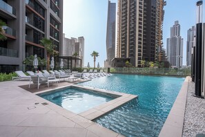 A swimming pool with lounge chairs and umbrellas, surrounded by high-rise buildings. - StayShort - 2 Bedroom in Business Bay Sleeps 6 with Water Canal Views! (Business Bay)