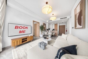 Ein modernes Wohnzimmer mit einer Couch, einem Couchtisch und einem Fernseher, der 'BOOK ME' anzeigt.