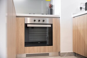 Una cocina con horno de acero inoxidable integrado, armarios de madera y encimera blanca.