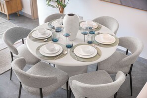 A round dining table with a white tablecloth, surrounded by six grey upholstered chairs. - StayShort - 2 Bedroom in Business Bay Sleeps 6 with Water Canal Views! (Business Bay)