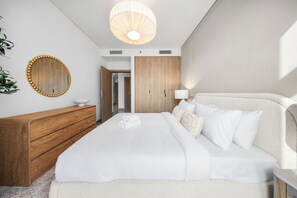 A modern bedroom with a large bed, wooden dresser, and a mirror on the wall. - StayShort - 2 Bedroom in Business Bay Sleeps 6 with Water Canal Views! (Business Bay)