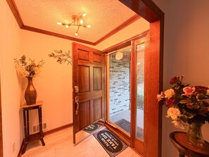 A wooden door with a glass panel, a doormat with text, and a vase with flowers.