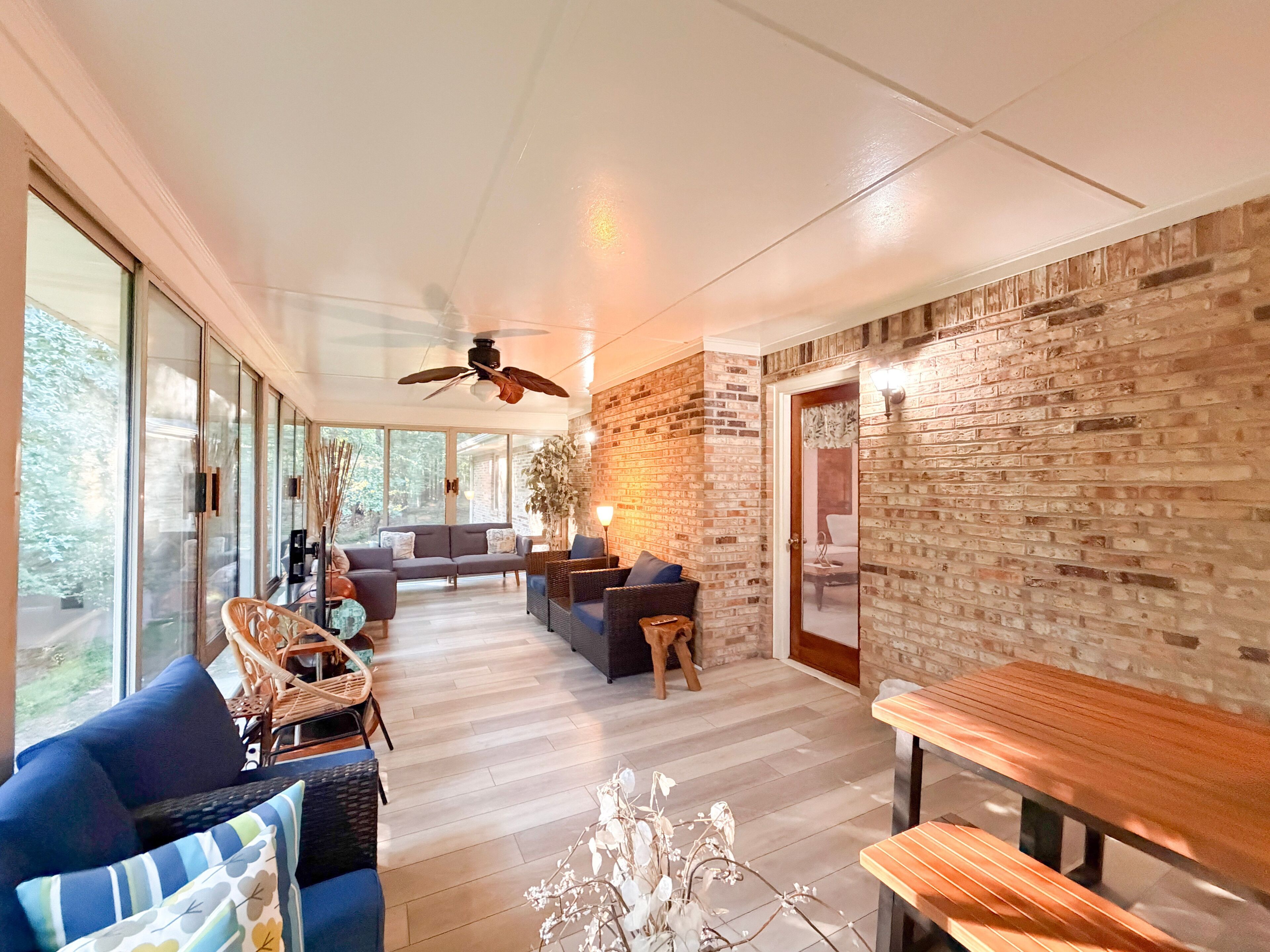 A spacious living area with a large window, a ceiling fan, and a brick wall.