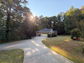 A residential house with a driveway leading to a garage, surrounded by trees and a well-maintained lawn.