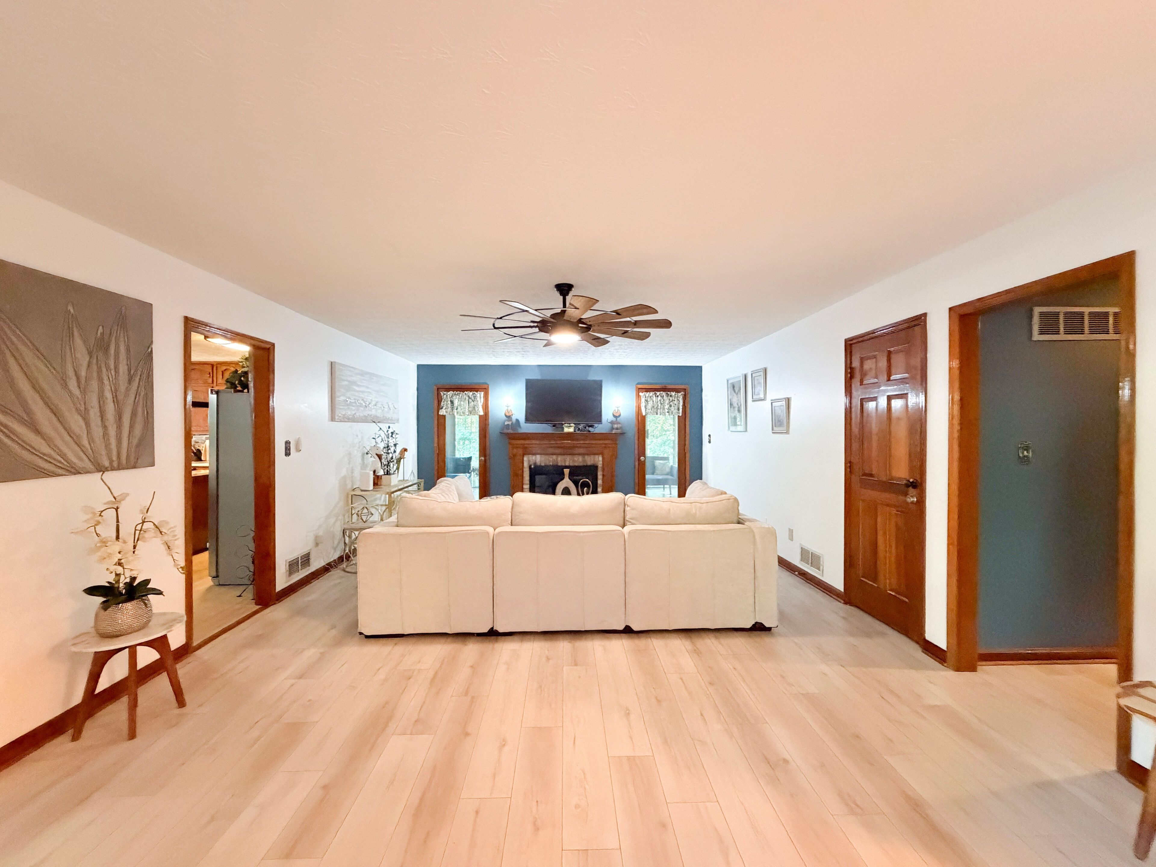 Un salon spacieux avec un grand canapé d’angle, une cheminée et un ventilateur de plafond.