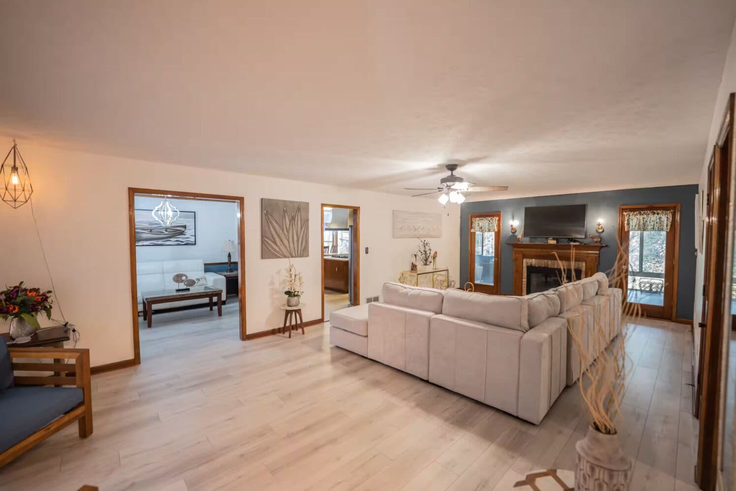 A spacious living room with a large sofa, a television, and a fireplace. There is a dining area with a table and chairs, and a kitchen in the background.