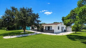 A single-story white building with a flat roof, surrounded by a well-maintained lawn and large trees. - NEW! Pool,  Pingpong, Foosball - Sleeps 10 (Largo)