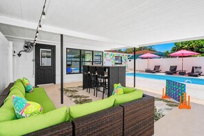 A covered outdoor area with a pool, lounge chairs, a dining set, and a door leading to the interior.