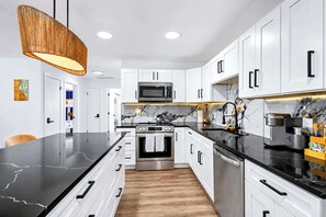 A modern kitchen with white cabinets, black countertops, and a central island.