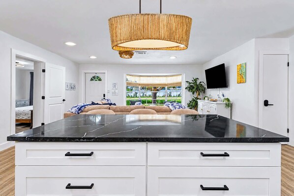 A modern kitchen with a large island, white cabinetry, and a hanging light fixture.