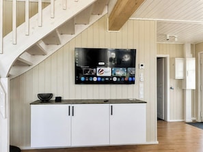 Eine moderne Küche mit integriertem Fernseher, weißen Schränken und einer Holztreppe.