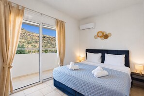 A hotel room with a bed, a view of the outdoors, an air conditioning unit, and a decorative wall piece. - Villa Starlight - Five Bedroom Villa, Sleeps 11 (Lardos)