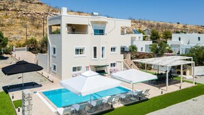 Un bâtiment moderne à deux étages doté d’une piscine, d’un espace extérieur aménagé et offrant une vue sur une colline.