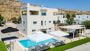 A modern two-story building with a swimming pool, outdoor seating, and a view of a hillside. - Villa Starlight - Five Bedroom Villa, Sleeps 11 (Lardos)