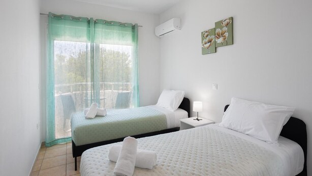 Une chambre d’hôtel avec deux lits, un balcon, une fenêtre avec des rideaux, un appareil de climatisation et une œuvre d’art accrochée au mur.