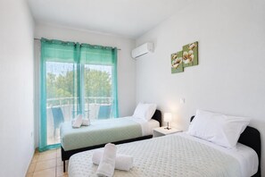Ein Hotelzimmer mit zwei Betten, einem Balkon und Blick auf Bäume.
