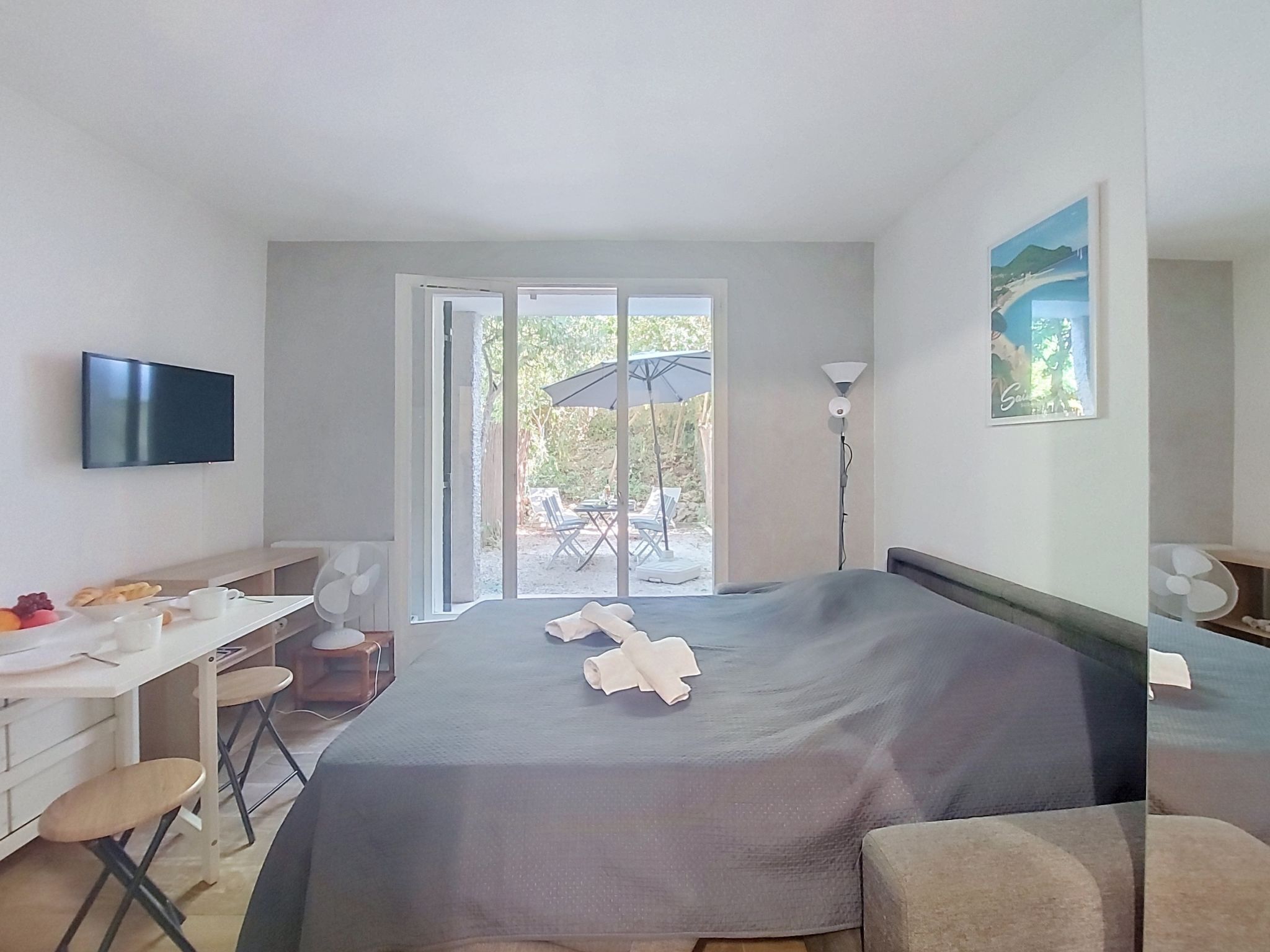 A hotel room with a bed, a desk, a chair, a TV, and a view of the outdoors.