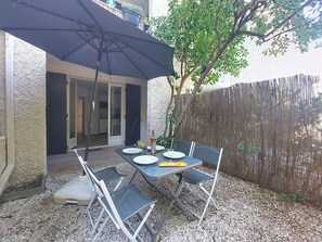 Eine Terrasse im Freien mit einem Tisch für zwei Personen, umgeben von Stühlen, unter einem großen Sonnenschirm.
