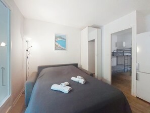 A bedroom with a bed, a bedside lamp, a painting, and a view of a kitchen area. - Les Aigues Marines by Interhome (Saint Cyr sur Mer La Madrague)
