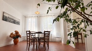 Un área de comedor con una mesa y sillas, una planta en maceta y una ventana con cortinas.
